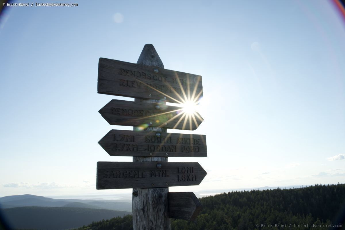 Trail signpost silhouetted with sunburst on Penobscot Mountain in Acadia National Park, Maine