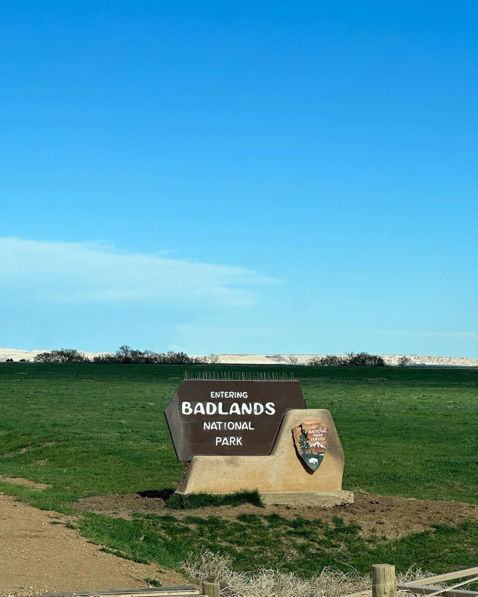 Entering Badlands National Park sign with green prairie and white rock formations on the horizon, South Dakota