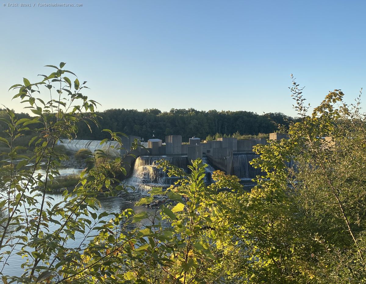 Water spilling over a stepped concrete dam at golden hour, framed by riverbank brush, Flint, Michigan