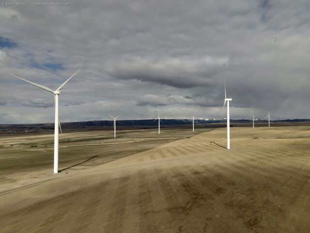 Aerial drone view of wind turbines standing over plowed fields under a storm sky, a snowcapped range on the horizon, Idaho