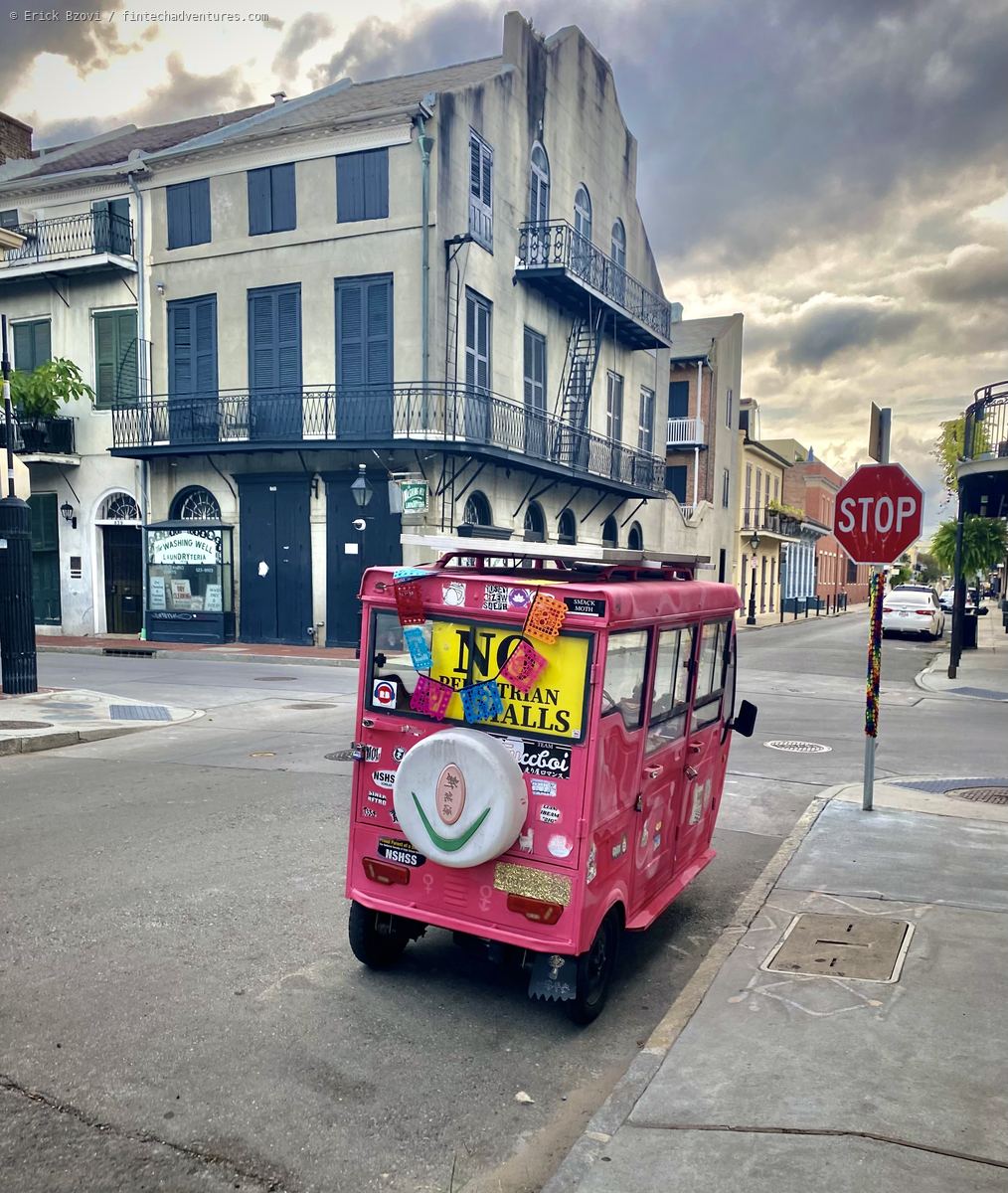 Pink electric tuk tuk parked at a French Quarter corner with wrought iron balconies and storm clouds overhead, New Orleans, Louisiana