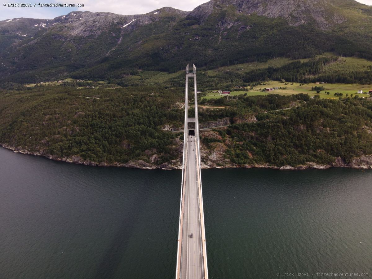 Aerial drone view of a suspension bridge spanning a Norwegian fjord with mountains rising behind