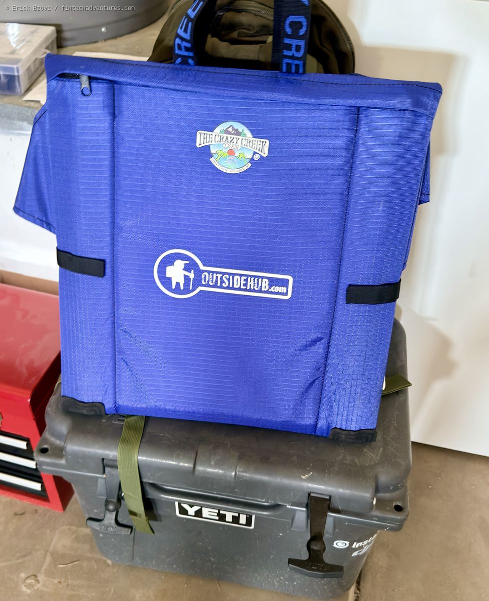 Crazy Creek folding camp chair printed with the OutsideHub.com logo, resting on a Yeti cooler in a garage