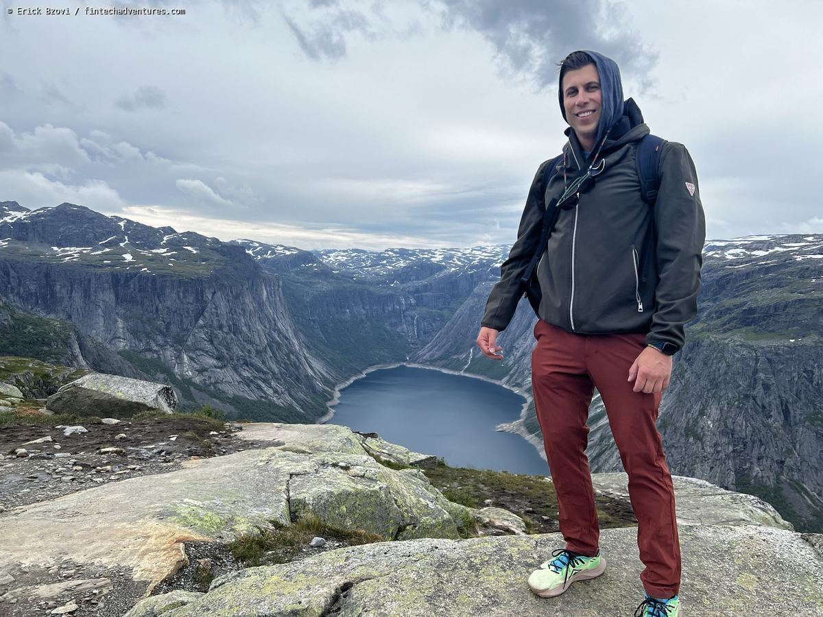 Standing at Trolltunga cliff above a glacial lake and snow-capped mountains in Norway